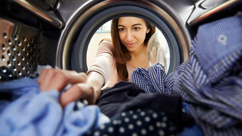 uma imagem de uma mulher a pôr roupa na máquina de lavar