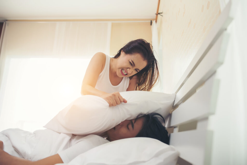 An image of a woman putting a pillow over her husband's mouth to stop his snoring