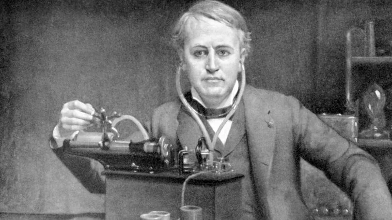 Uma fotografia a preto e branco de Thomas Edison em frente a uma máquina