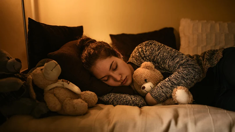 uma mulher dorme na cama com a luz acesa