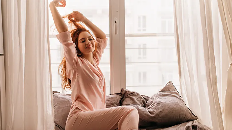 uma mulher de pijama que se estica em frente a uma janela