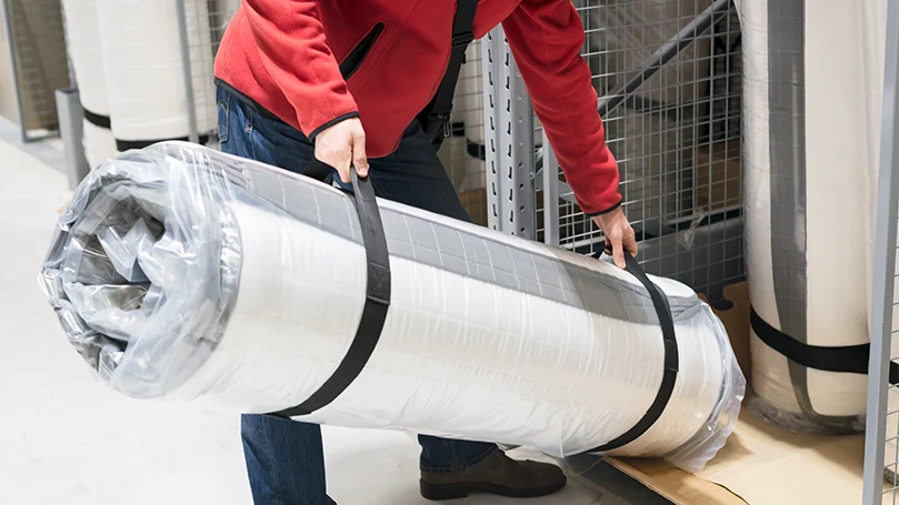 an image of a man holding a packed mattress