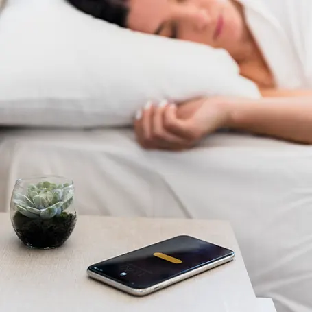 Uma imagem de uma mulher a dormir com o telemóvel na mesa de cabeceira