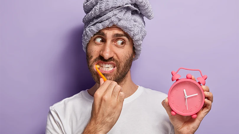 Uma imagem de um homem que acordou tarde a olhar para um relógio e a lavar os dentes