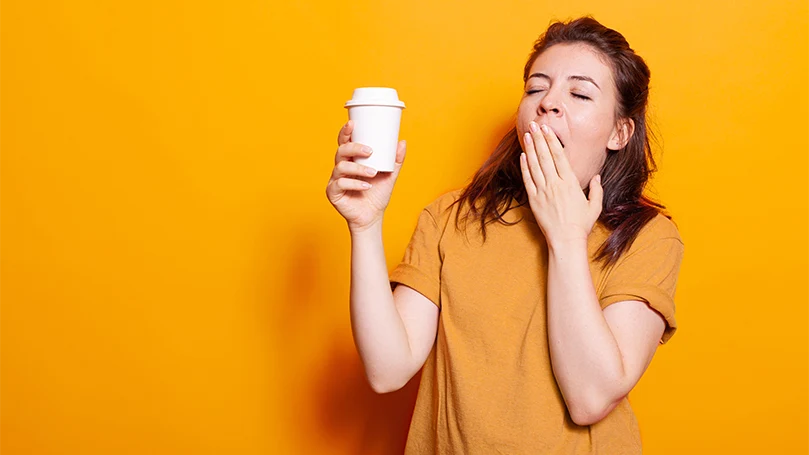 Uma mulher sonolenta com uma chávena de café na mão.