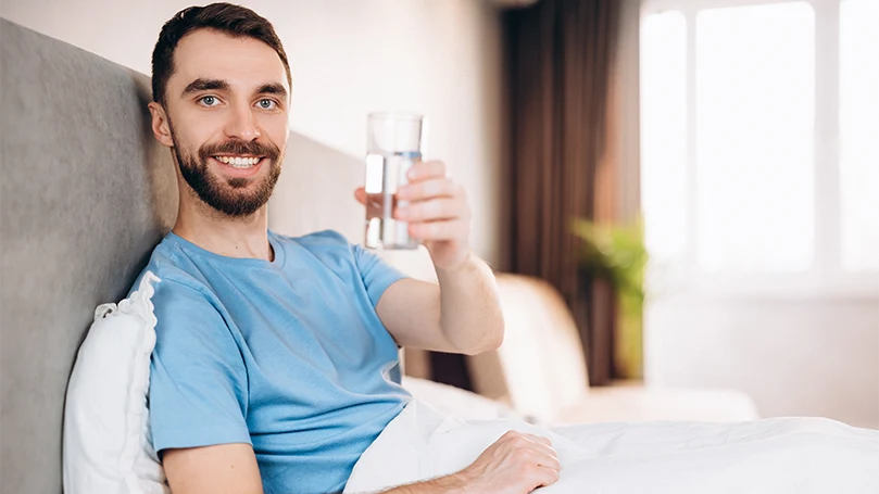 Uma imagem de um homem a beber um copo de água na sua cama antes de se deitar.