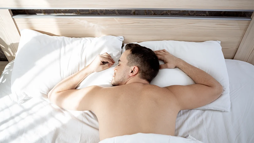 um homem a dormir de barriga para baixo na sua cama.