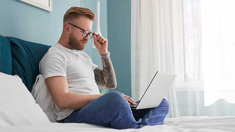 Uma imagem de um homem a trabalhar a partir de casa, na sua cama.