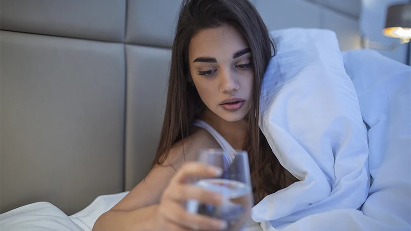 Uma imagem de uma jovem mulher a beber um copo de água na cama.