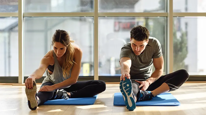 Imagem de um casal a alongar-se e a fazer exercício pela manhã.