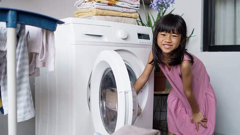 Uma imagem de uma menina a colocar um cobertor numa máquina de lavar.