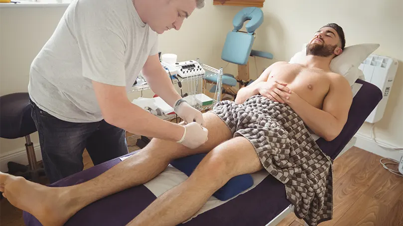 Imagem de um homem na terapia inclinada a receber uma massagem do fisioterapeuta.