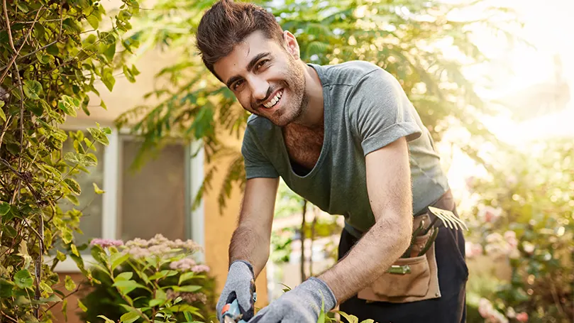 Uma imagem de um homem a trabalhar num jardim à luz do dia.