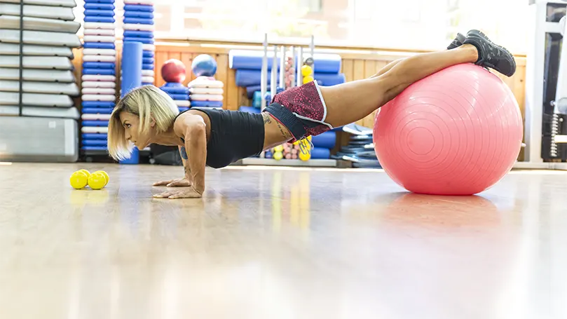 Uma imagem de uma mulher a fazer flexões em declive numa bola de ioga