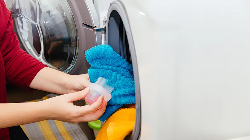 Uma imagem de uma mulher a deitar detergente numa máquina de lavar roupa.