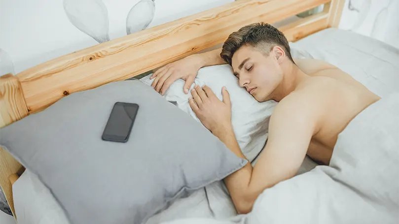 Uma imagem de um homem jovem e bonito a dormir profundamente na sua cama.