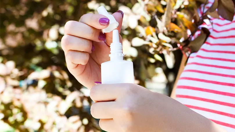 Uma mulher com um spray nasal na mão.