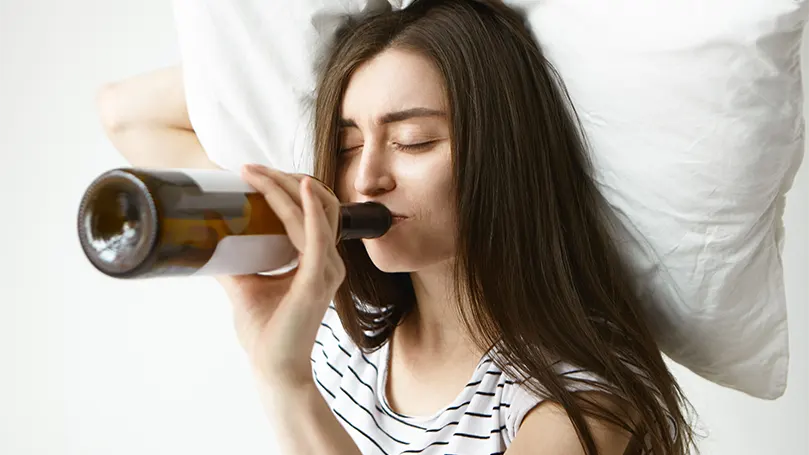 Uma imagem de uma mulher a beber álcool na cama.