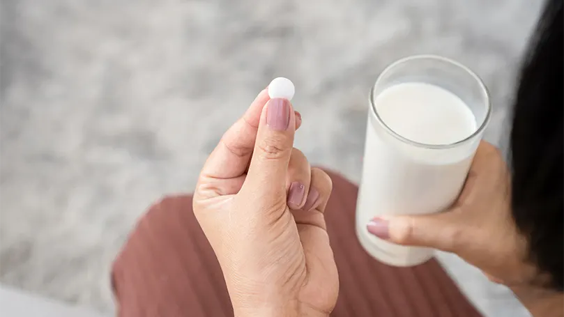 Uma mulher a tomar um comprimido de melatonina com um copo de leite.