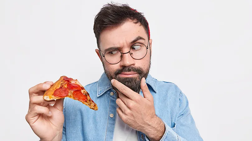 um homem barbudo segurando uma fatia de pizza