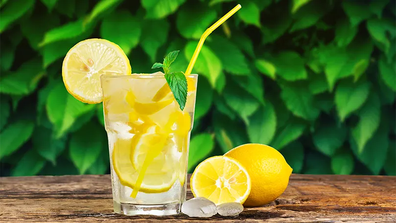 a glass of lemon water next to two lemons on a table.