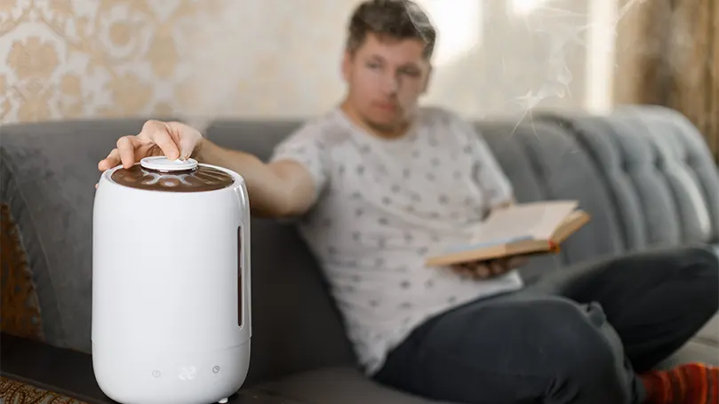 Um jovem a ler um livro no sofá e a preparar um humidificador