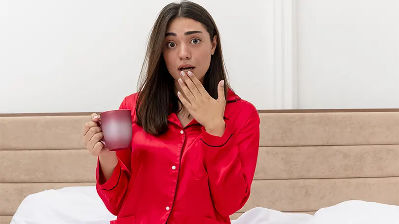 Uma imagem de uma mulher de pijama vermelho a beber água por ter acordado com a boca seca.