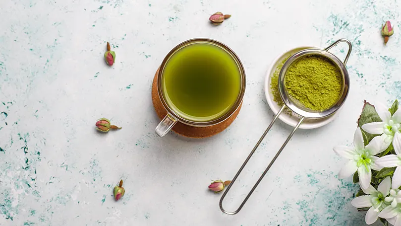 Uma imagem de pó de matcha junto a uma chávena de chá matcha