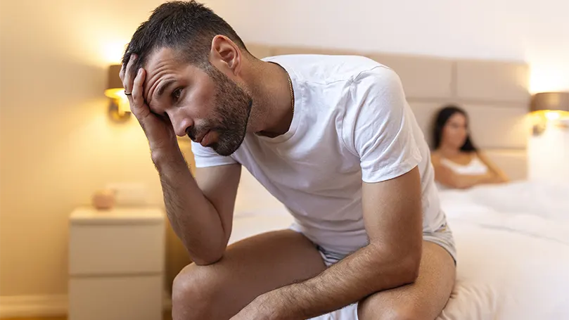 Uma imagem de um homem sentado na beira da cama.