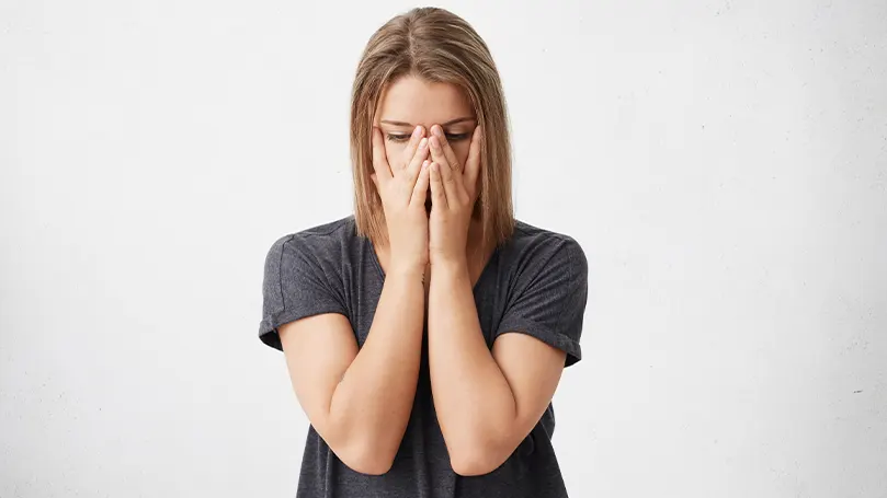 An image of a woman with her hands covering her face as she suffers from winter fatigue symptoms