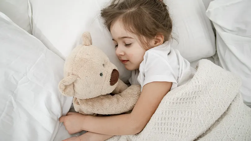 Imagem de uma menina aconchegada na cama com o seu animal de peluche