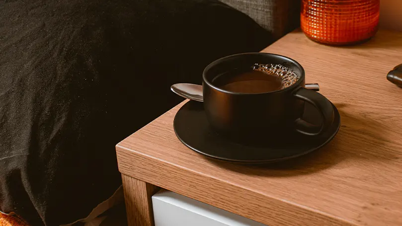 Uma imagem de uma mesa de cabeceira com uma chávena de café em cima.