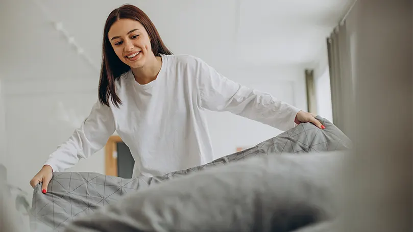 Uma imagem de uma mulher feliz a fazer a cama.