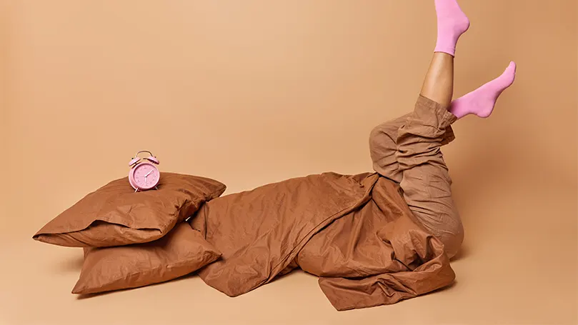 An image of a woman covered in a brown bed sheet and a small pillow