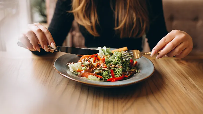 uma mulher sentada à mesa e a comer uma refeição saudável