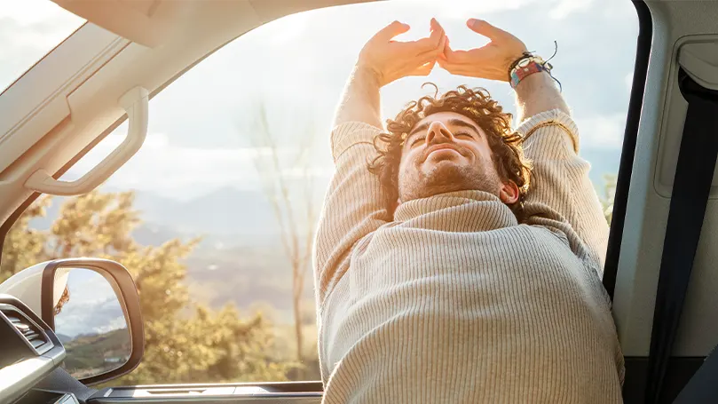 Imagem de um homem a esticar-se depois de dormir num carro.