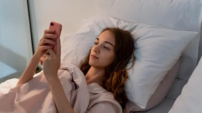 Uma imagem de uma jovem mulher na cama com um telemóvel na mão