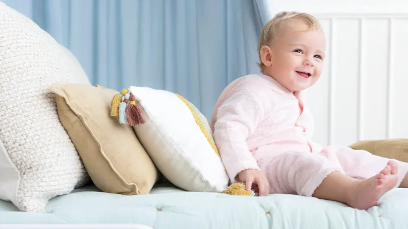 Uma imagem de uma criança sentada numa cama junto a algumas almofadas de criança